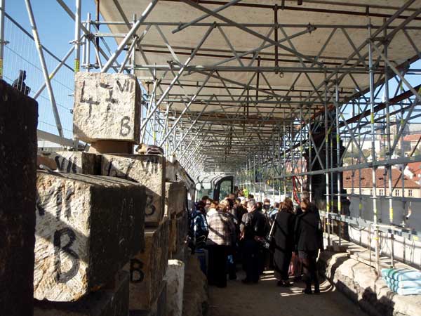 Skupiny návštěvníků procházejí stavbou podél označených pískovcových kvádrů ze zábradlí Karlova mostu
